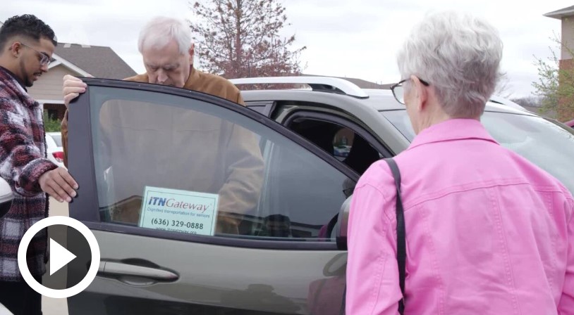 young man helping older man out of car with older woman facing them